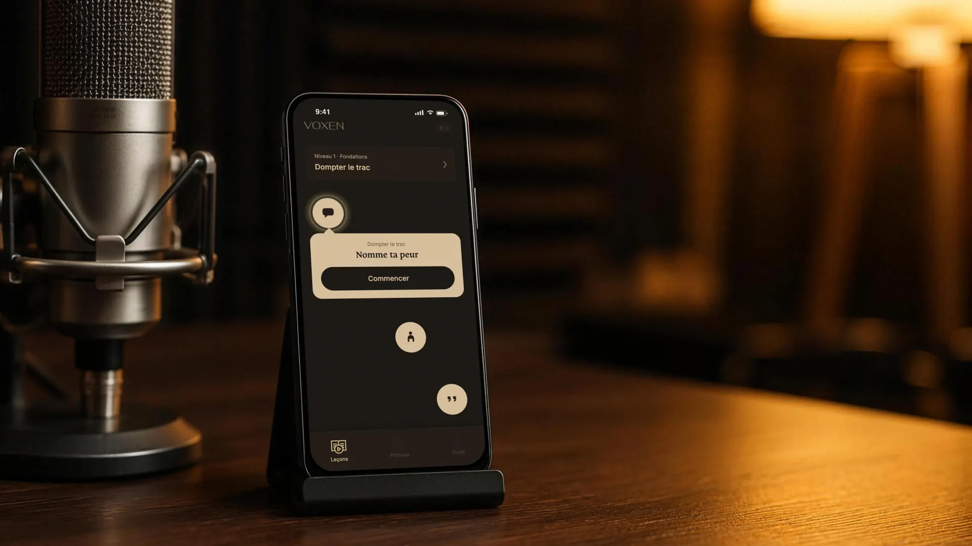 Un iPhone dans son support, à côté d’un micro de studio. À l’écran, Voxen&nbsp;: la leçon «&nbsp;Dompter le trac&nbsp;» et l’exercice «&nbsp;Nomme ta peur&nbsp;».
